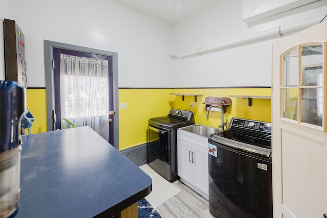 clothes washing area featuring a sink, light wood-type flooring, cabinet space, and washing machine and clothes dryer