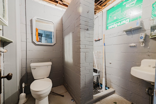 bathroom featuring toilet and concrete block wall