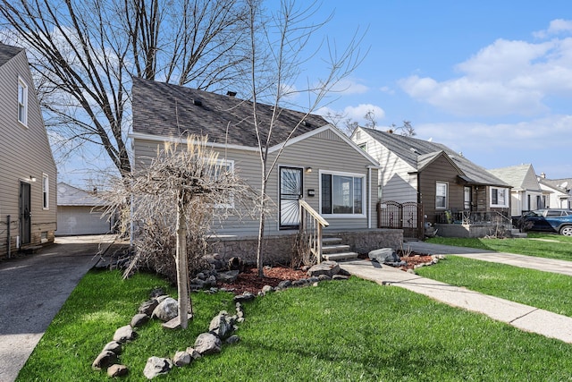 bungalow-style house with a garage, a shingled roof, a front yard, and an outdoor structure