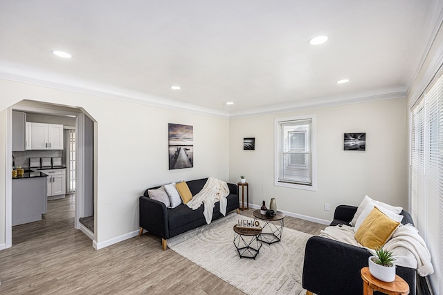 living room with light wood-style flooring, baseboards, arched walkways, and ornamental molding