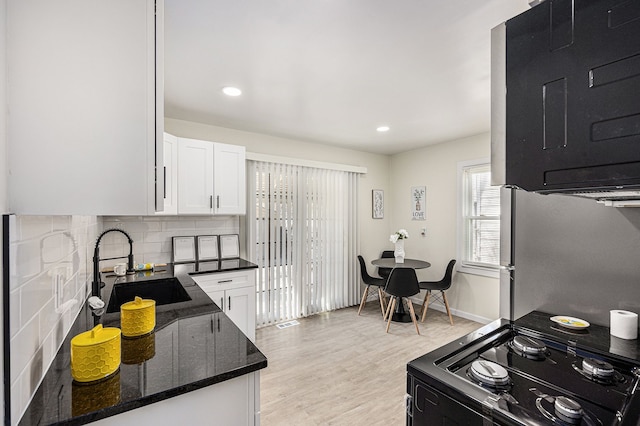 kitchen with dark stone counters, freestanding refrigerator, white cabinets, black / electric stove, and a sink