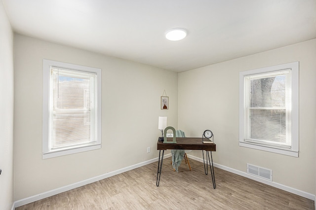 office space featuring light wood-style flooring, baseboards, visible vents, and a wealth of natural light