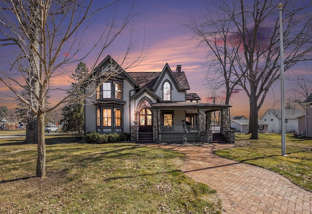 view of front facade featuring a porch, a yard, and a chimney