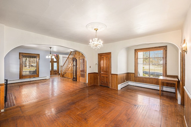 empty room featuring arched walkways, a notable chandelier, wainscoting, and a baseboard heating unit