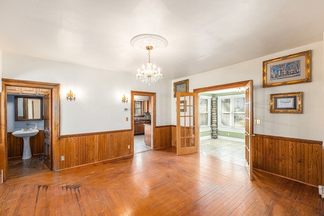 unfurnished dining area with hardwood / wood-style floors, an inviting chandelier, a wainscoted wall, and wood walls