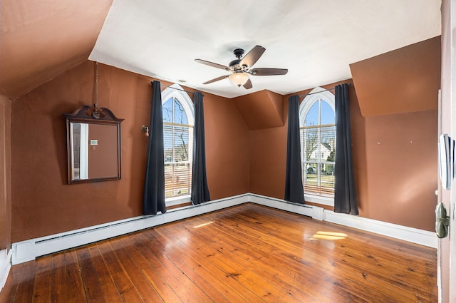 spare room featuring lofted ceiling, baseboard heating, hardwood / wood-style floors, and a ceiling fan