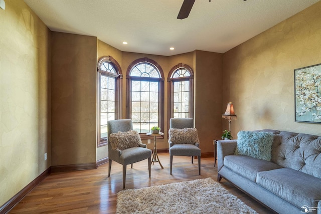 living area with wood finished floors, baseboards, ceiling fan, a textured ceiling, and a textured wall