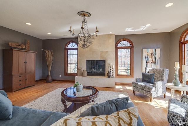 living area featuring baseboards, a chandelier, a tiled fireplace, recessed lighting, and light wood-style floors