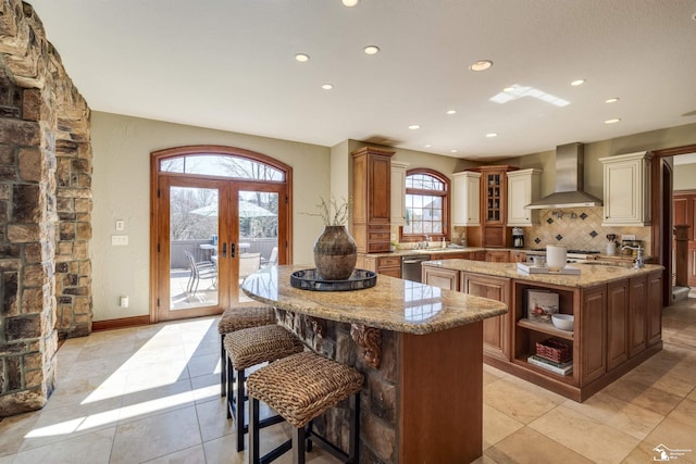 kitchen featuring light stone countertops, a kitchen island, decorative backsplash, appliances with stainless steel finishes, and wall chimney exhaust hood