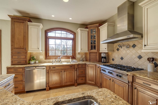 kitchen with a sink, light stone counters, backsplash, appliances with stainless steel finishes, and wall chimney exhaust hood