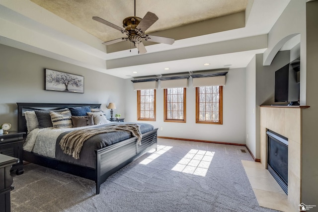 bedroom featuring a fireplace with flush hearth, light colored carpet, baseboards, and a tray ceiling