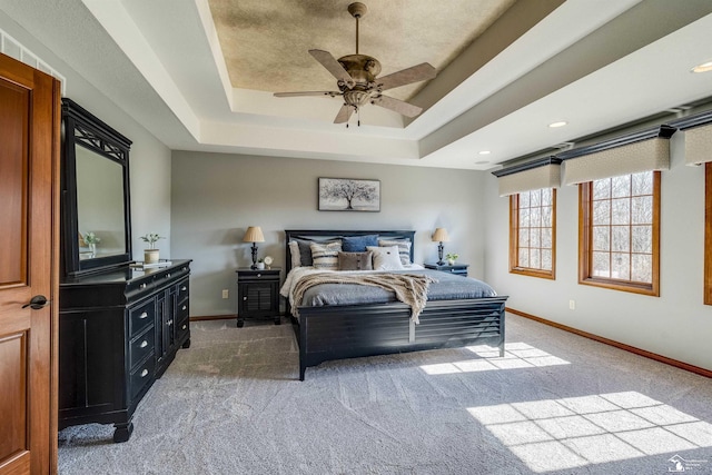 bedroom featuring a raised ceiling, a ceiling fan, baseboards, and light carpet