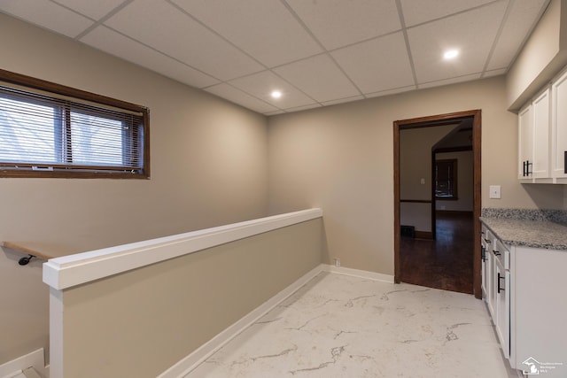 interior space featuring baseboards, recessed lighting, white cabinets, marble finish floor, and a paneled ceiling