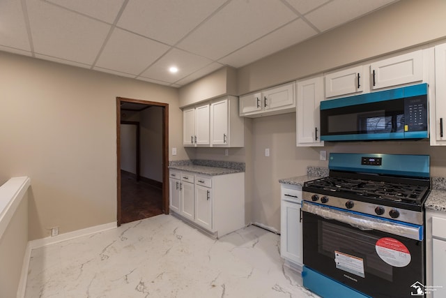 kitchen featuring stainless steel range with gas cooktop, baseboards, a drop ceiling, light stone counters, and white cabinetry