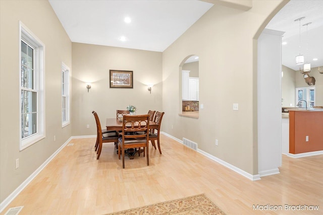 dining space with baseboards, light wood-style floors, visible vents, and arched walkways