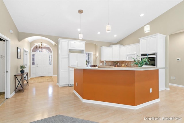 kitchen with white appliances, white cabinets, arched walkways, and lofted ceiling