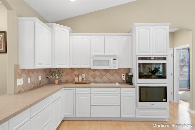 kitchen with lofted ceiling, light wood-style flooring, arched walkways, white cabinets, and white appliances