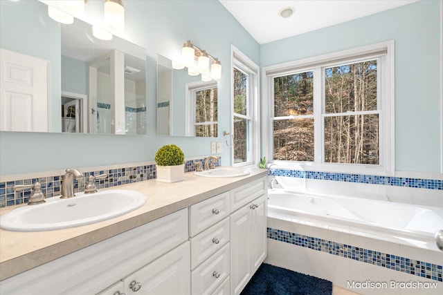 bathroom with a garden tub, double vanity, tasteful backsplash, and a sink