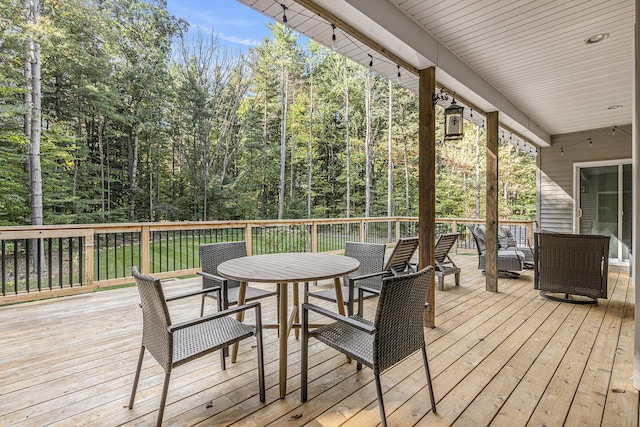 wooden terrace featuring outdoor dining area and a view of trees