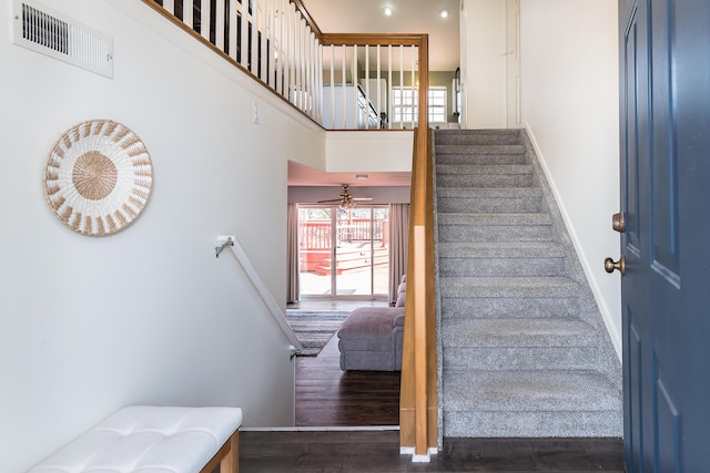 stairs featuring visible vents, a high ceiling, baseboards, and wood finished floors