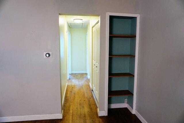 corridor with built in features, attic access, baseboards, and wood finished floors