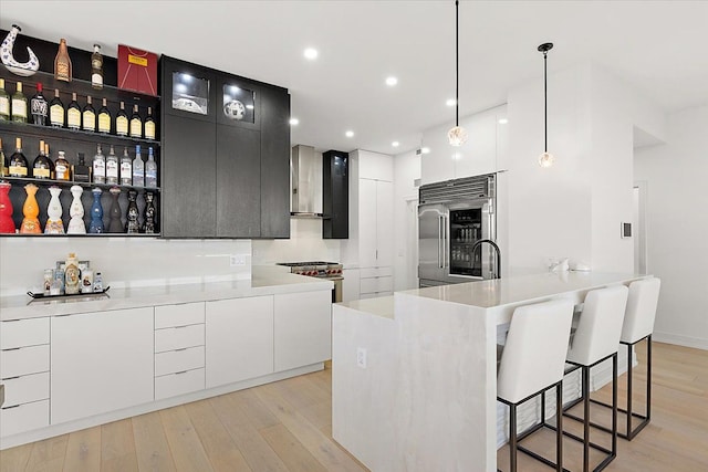 kitchen featuring wall chimney range hood, modern cabinets, premium appliances, and light wood finished floors