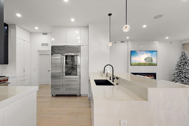 kitchen featuring a sink, light wood-type flooring, white cabinetry, high end appliances, and modern cabinets