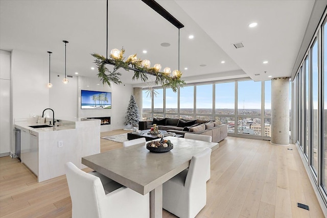 dining area with visible vents, a warm lit fireplace, floor to ceiling windows, and light wood finished floors