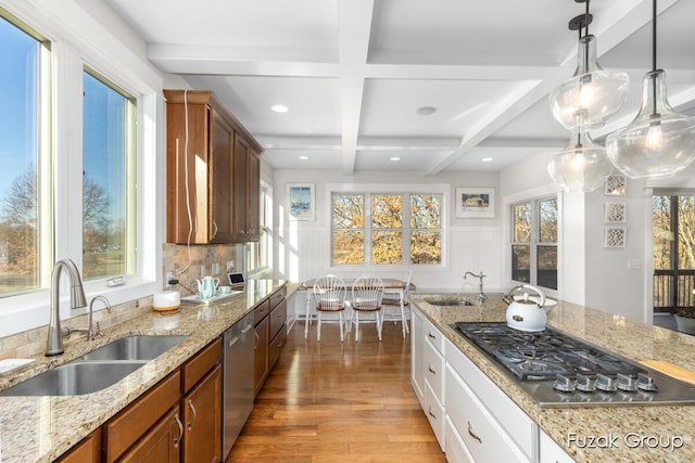 kitchen featuring light wood finished floors, coffered ceiling, stainless steel appliances, and a sink