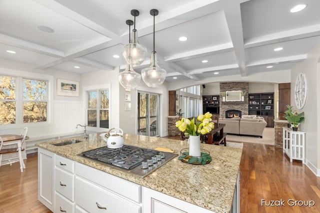 kitchen with a sink, wood finished floors, coffered ceiling, and stainless steel gas cooktop