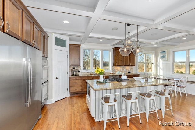 kitchen featuring light stone counters, stainless steel appliances, light wood-style floors, and brown cabinetry