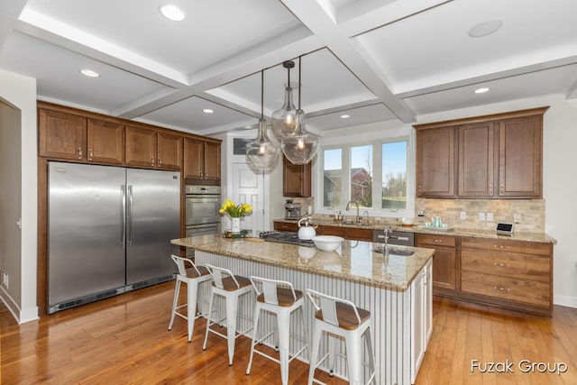 kitchen with backsplash, an island with sink, coffered ceiling, and appliances with stainless steel finishes