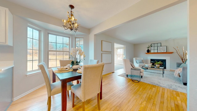 dining room with a fireplace, a notable chandelier, a healthy amount of sunlight, and light wood-style floors