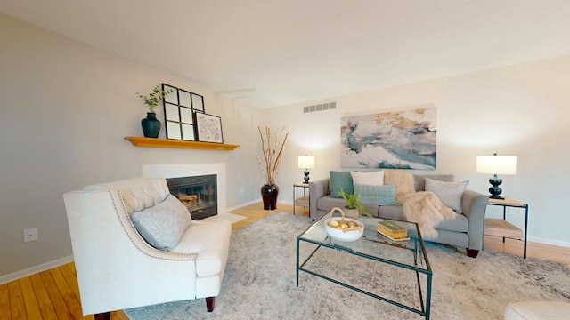 living area with a fireplace with flush hearth, wood finished floors, visible vents, and baseboards