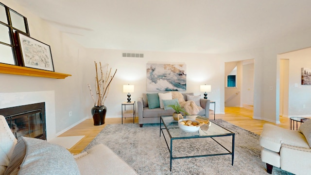 living room with visible vents, baseboards, a glass covered fireplace, and wood finished floors