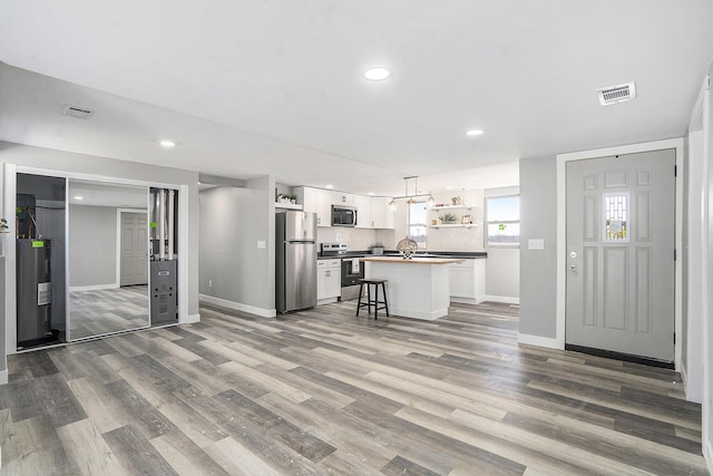 unfurnished living room with visible vents, electric water heater, baseboards, recessed lighting, and wood finished floors