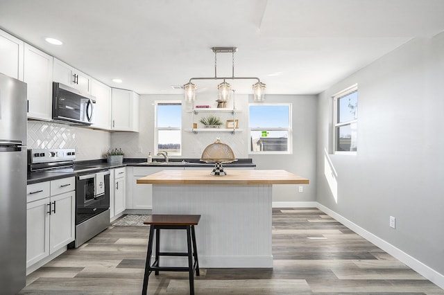 kitchen with a healthy amount of sunlight, butcher block countertops, stainless steel appliances, white cabinets, and backsplash