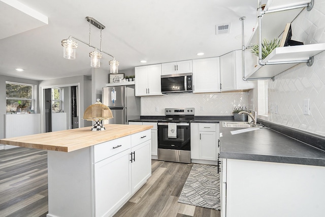 kitchen with wooden counters, a sink, stainless steel appliances, white cabinets, and a center island