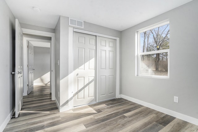 unfurnished bedroom featuring visible vents, baseboards, a closet, and wood finished floors