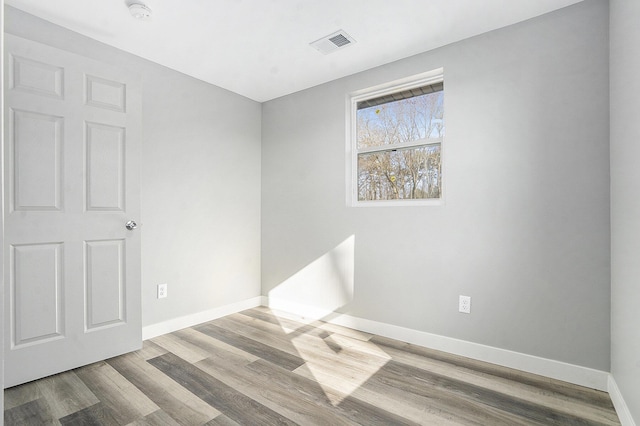 empty room featuring wood finished floors, visible vents, and baseboards