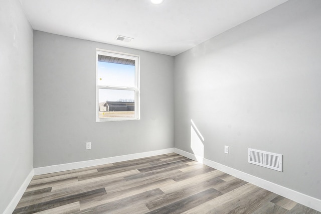 spare room featuring wood finished floors, visible vents, and baseboards