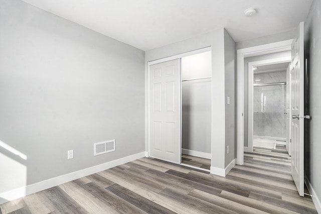 unfurnished bedroom featuring visible vents, baseboards, a closet, and wood finished floors