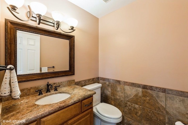 bathroom with wainscoting, vanity, toilet, and tile walls