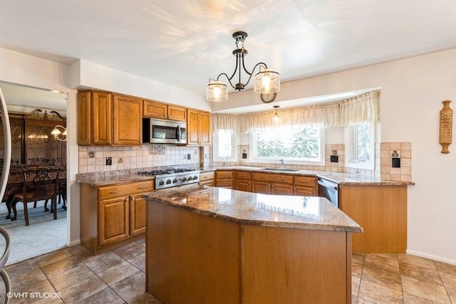 kitchen with backsplash, a chandelier, light stone counters, appliances with stainless steel finishes, and a sink