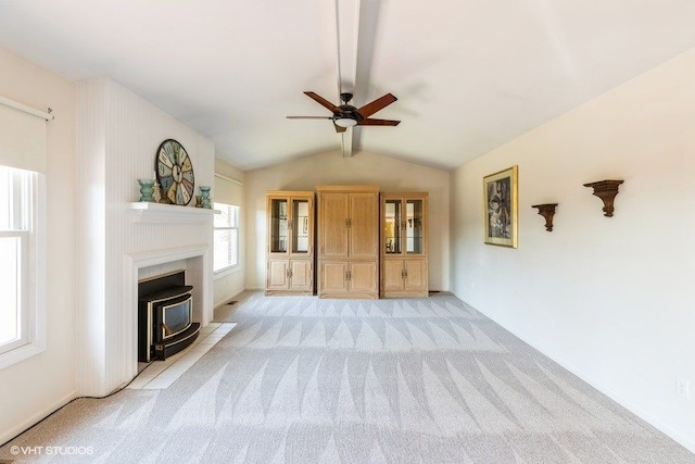 unfurnished living room with a wood stove, light colored carpet, ceiling fan, and vaulted ceiling with beams