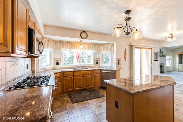 kitchen featuring brown cabinets, a sink, appliances with stainless steel finishes, tasteful backsplash, and a center island