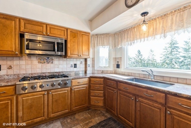 kitchen with tasteful backsplash, light stone counters, brown cabinetry, stainless steel appliances, and a sink