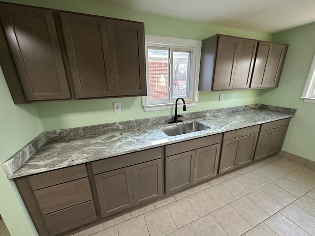 kitchen with light tile patterned flooring, light stone countertops, baseboards, and a sink