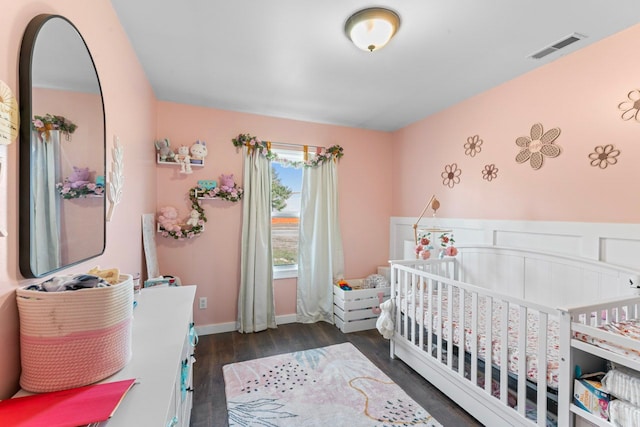 bedroom with visible vents, a crib, and wood finished floors