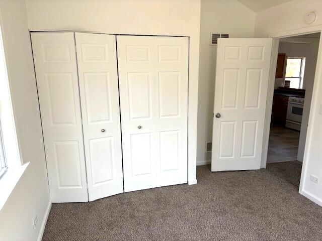 unfurnished bedroom featuring visible vents, a closet, dark carpet, and baseboards